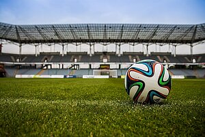 Ein Fußball liegt auf dem Spielfeld. Man sieht das leere Stadion im Hintergrund