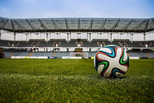 Ein Fußball liegt auf dem Spielfeld. Man sieht das leere Stadion im Hintergrund 