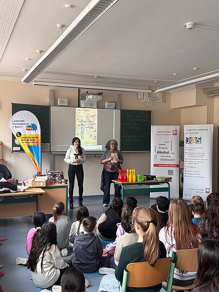 Lesung in Ingolstadt: Mein Papa, die Unglücksspiele und ich

Während der COA‑Aktionswoche las Autorin Gundi Herget gestern an der Grundschule „Auf der Schanz“ in Ingolstadt aus ihrem Buch „Mein Papa, die Unglücksspiele und ich“. Organisiert wurde die Lesung von der Fachstelle Glücksspielsucht der Caritas‑Suchtambulanz Ingolstadt in Kooperation mit der Jugendsozialarbeit an Schulen der Caritas-Kreisstelle Ingolstadt und der Landesstelle Glücksspielsucht in Bayern. Die Aktionswoche wird jährlich von NACOA Deutschland initiiert.

Das Buch erzählt die Geschichte der zehnjährigen Alina, die entdeckt, dass ihr Sparschwein geplündert wird. Gemeinsam mit ihrem Freund Pepe und dessen Detektivkoffer sucht sie nach dem Täter – möglicherweise ihr Vater, der seine Glücksspielsucht finanzieren will.

Herget las mit viel Einfühlungsvermögen und half den rund 75 Kindern der dritten und vierten Klassen, Alinas Gefühle und Herausforderungen nachzuvollziehen. Durch die Zusammenarbeit mit Marie Lehner, Inhaberin der Fachstelle Glücksspielsucht, flossen wichtige Informationen zu pathologischem Glücksspiel ein. Die Lesung war interaktiv gestaltet: Mit Fragen und kurzen Diskussionsrunden wurden die Kinder aktiv einbezogen. Herget vermittelte das schwierige Thema verständlich und zugleich fesselnd.

Im Anschluss stellten die Kinder Fragen und vertieften das Thema weiter. „Die Veranstaltung hat bei den Kindern sicher bleibende Eindrücke hinterlassen. Sie haben erfahren, dass es immer Wege gibt, mit belastenden Situationen umzugehen und Hilfe zu finden“, resümiert Marie Lehner.

Während der COA‑Aktionswoche rücken Kinder aus suchtbelasteten Familien in den Mittelpunkt. Mehr als 2,6 Millionen Kinder in Deutschland sind betroffen. Die Landesstelle Glücksspielsucht in Bayern koordiniert bayernweit Prävention, Forschung, Beratung und Hilfe zum Thema pathologisches Glücksspiel.

Hier erfahren Sie mehr über das Buch, das bei uns kostenlos erhältlich ist: 
https://www.lsgbayern.de/kinderbuch

Foto: Gundi Herget liest Grundschulkindern aus ihrem Buch. Mit im Bild ist Marie Lehner. Foto: Sandra Daniel/Caritas